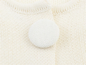 Macro shot of cream knit cardigan featuring delicate woven fabric buttons and fine texture