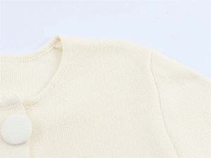 Detailed close-up of cream knit cardigan featuring a large fabric-covered button and collar