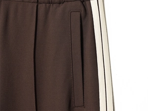 Detailed close-up of dark brown sweatpants featuring cream side stripes and pocket seams