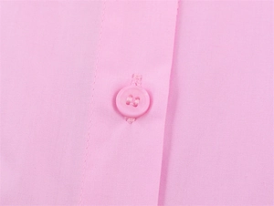Macro detail of a pink poplin shirt featuring a matching resin button and neat stitching