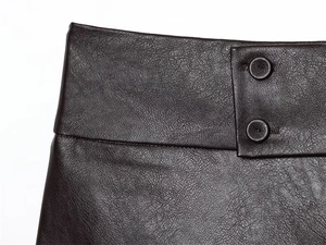 Dettaglio pantaloncini in pelle marrone scuro con vita alta e doppi bottoni verticali
