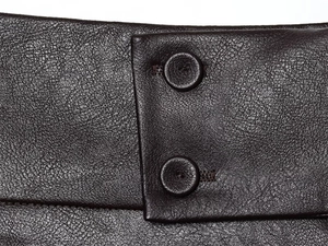 Dettaglio dei pantaloncini marroni gessati in pelle a grana fine con due bottoni coordinati