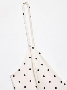Detailed close-up of the thin strap and black polka dot pattern on an off-white romper