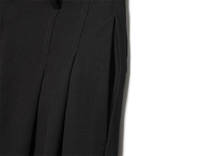 Détail du pantalon plissé noir avec poche latérale et coutures de précision soignées