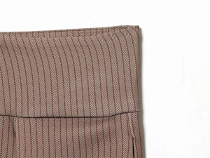 Détail macro du pantalon à pinces à chevrons marron et rouge montrant la coupe de taille