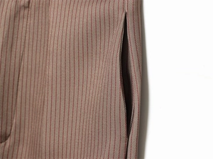 Détail macro du pantalon ballon à chevrons rouge-brun montrant la couture de la poche