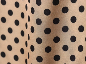 Detail of champagne gold satin fabric with black polka dots and smooth texture