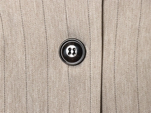 Detail eines Fischgräten-Blazers mit dunkelbraunem Knopf und feinem Nadelstreifen-Muster