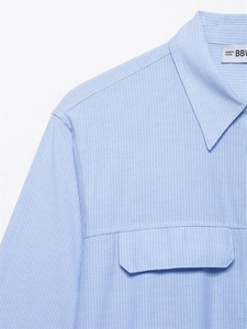 Dettaglio della camicia a righe azzurre con colletto a punta e tasca a pattina cucita