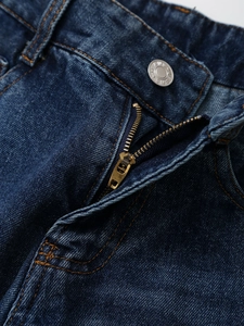 Detailaufnahme des Metallknopfes, Reißverschlusses und der orangen Nähte der blauen Jeans