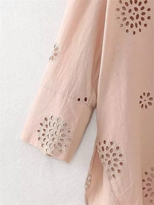 Dettaglio del ricamo floreale traforato rosa su una camicia estiva in cotone leggero