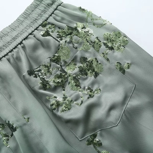 Detailed view of elastic waistband and floral sequin embroidery on satin trousers