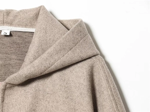 Dettaglio del colletto della giacca beige con cappuccio con etichetta S e trama morbida