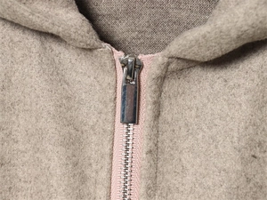 Dettaglio giacca con cappuccio beige con nastro zip rosa e cursore in metallo