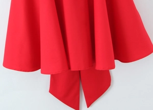 Detail view of a vibrant red mini dress featuring a large decorative bow and stylish wavy hem