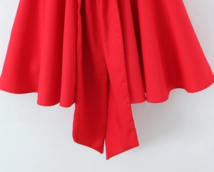 Close-up detail of a vibrant red mini dress featuring a large decorative bow and pleated hem.