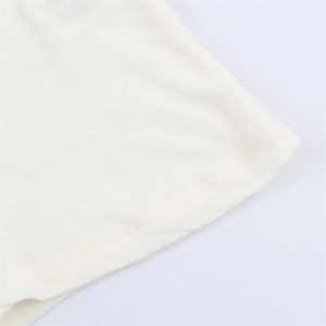 Dettaglio ravvicinato della cucitura pulita sull'orlo della t-shirt asimmetrica crema