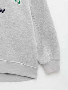 Gros plan sur le tissu gris du sweat avec broderie colorée et poignets en maille côtelée