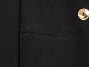 Detail of black woven jacket fabric featuring a pocket and a gold button with texture