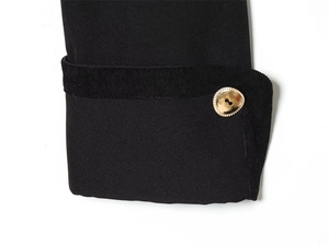 Close-up of black jacket cuff featuring textured gold button and velvet trim detail