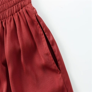 Détail de la taille élastiquée à plis et des poches latérales sur le pantalon en satin rouge
