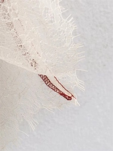 Macro detail of white eyelash lace trim featuring decorative red contrast stitching line