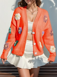 Détail d'un cardigan en maille orange vif avec des fleurs tricotées en 3D et un décolleté en V