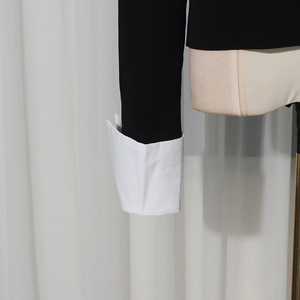 Dettaglio della manica in maglia a contrasto con polsino bianco ripiegato su un top