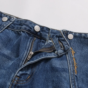 Dettaglio vita dei jeans con doppi bottoni, cerniera YKK e ricamo giallo decorativo