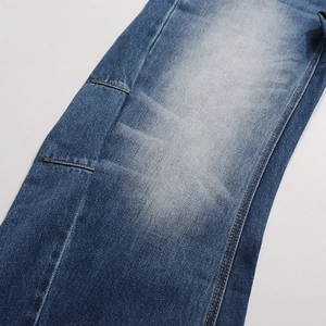 Dettaglio dei pantaloni in denim blu medio con lavaggio moustaches e cuciture a contrasto
