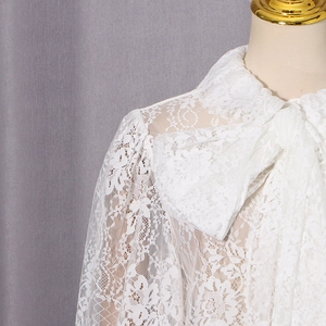 Détail du chemisier en dentelle blanche avec grand nœud papillon et poignets fins