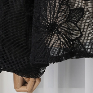 Détail macro d'une broderie florale noire sur un tissu en maille transparente de la manche