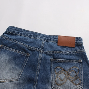 Dettaglio dei jeans blu scuro con ricamo giallo e toppa in pelle vintage sulla vita