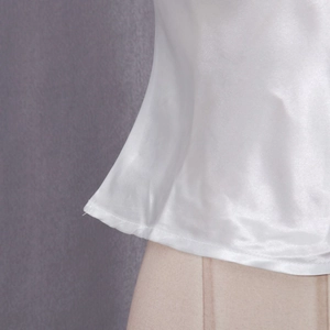Detailed view of white satin shirt hem with premium stitching on a grey background