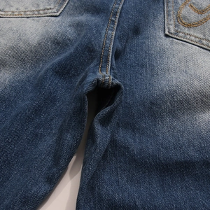 Dettaglio di jeans blu scuro che mostra cuciture rinforzate e ricamo a onde arancioni