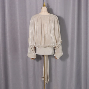 Detail of champagne pleated blouse featuring lantern sleeves and flowing silk ribbon ties