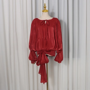 Detail of burgundy satin blouse showing textured pleated fabric and large bow tied at waist