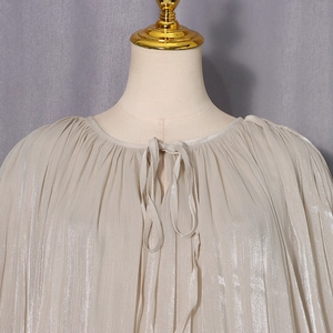 Detail view of champagne pleated blouse with elegant ribbon tie and metallic silk texture