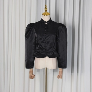 Detail of black satin blouse featuring puff sleeves and elegant peplum hemline
