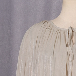 Detailed view of champagne pleated satin shirt with elegant neck tie and metallic sheen