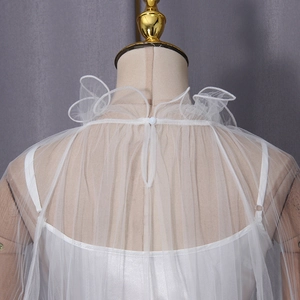 Detail of white sheer mesh cape featuring ruffled stand collar and back button closure