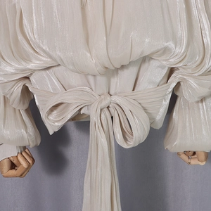 Detail of elegant champagne pleated fabric shirt featuring a large waist bow tie design