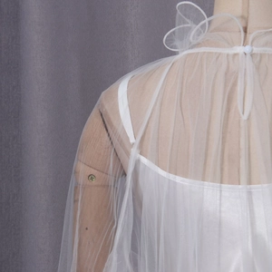Detail of white sheer mesh shawl featuring a delicate button closure and layered lace design