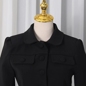 Detail of black fitted blazer featuring small lapels, button closure and pocket flaps