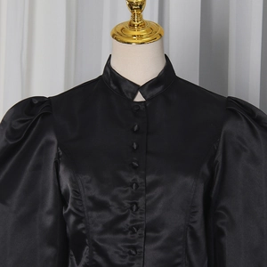 Detail of mandarin collar with fabric-covered buttons and puff sleeves on black satin shirt