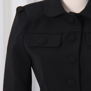 Detail of black blazer featuring round collar, fabric buttons and flap chest pockets