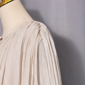 Detailed close-up of champagne pleated chiffon fabric texture and shoulder folds