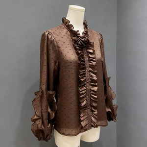 Detail of ruffle collar and 3D rose decor on a brown polka dot blouse with long sleeves