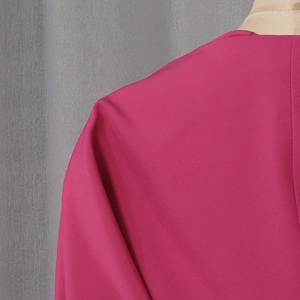 Detailed close-up of flamingo pink fabric shoulder seams and woven texture on a slim V-neck top