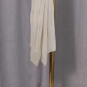 Detail showing vertical pleats on a beige long-sleeve shirt with silky texture and sheen